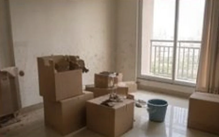 A dusty empty room with stacked moving boxes and stained walls